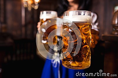 Young Oktoberfest waitress, wearing a traditional Bavarian dress, serving big beer mugs at bar. Stock Photo