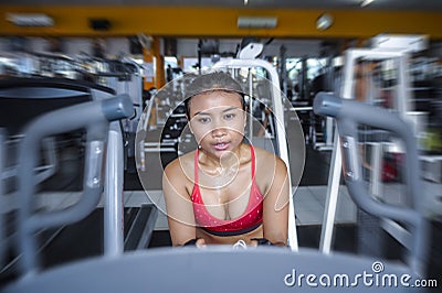 and sweaty Asian woman training hard at gym using elliptical pedaling machine gear in intense workout Stock Photo