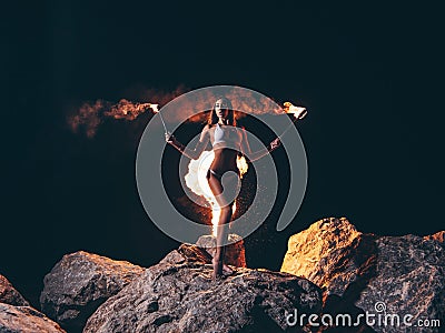 Young sexy woman with a gorgeous slim body in bikini is staying posing at the dark night on the rock with the lit by fire torche Stock Photo