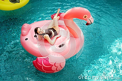 Young and sexy woman, having fun and laughing on an inflatable giant pink flamingo in the pool Float air mattress in a bikini Stock Photo