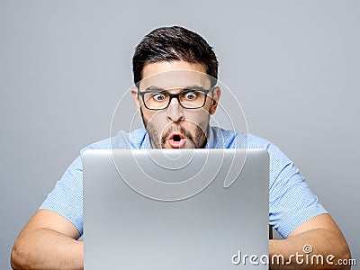 Young shocked man in blue shirt using laptop Stock Photo