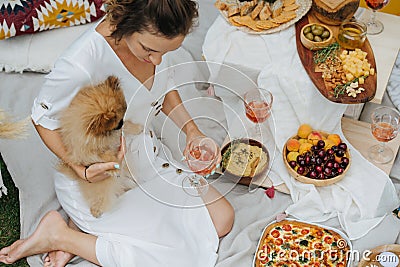 Young woman at a picnic on lawn with a small dog, next to appetizer table Stock Photo