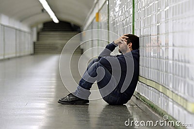 Young sick man lost suffering depression sitting on ground street subway tunnel Stock Photo