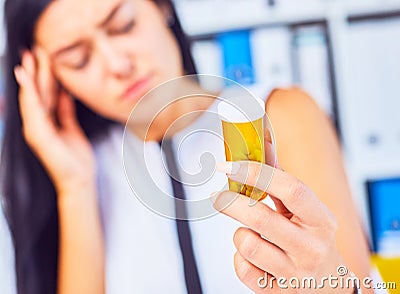 Young sick tired sad woman sitting in workplace holding bottle with pills. Female feeling bad at work. Stock Photo