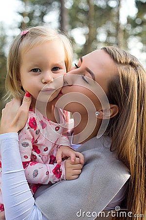 Young mother holding cute toddler girl daughter in her arms and giving her a kiss on a cheek Stock Photo