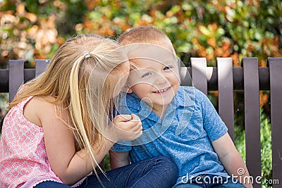 Young Sister and Brother Whispering Secrets On a Bench At The Stock Photo