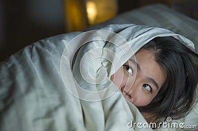 Young sleepless beautiful and scared Asian Chinese woman lying on bed awake at night suffering nightmare after watching zombie Stock Photo