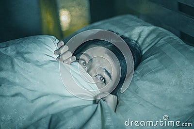 Young sleepless beautiful and scared Asian Japanese woman lying on bed awake at night suffering nightmare after watching zombie Stock Photo