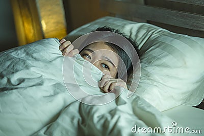 Young sleepless beautiful and scared Asian Korean woman lying on bed awake at night suffering nightmare after watching zombie Stock Photo