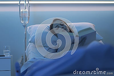Young sleepless patient lying in the hospital bed and reading a book Stock Photo