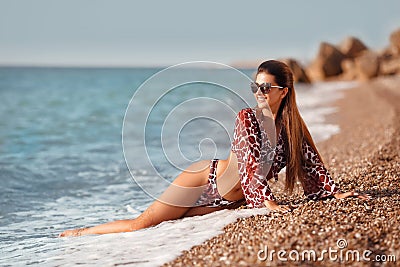Young slender girl in bikini swimwear sunbathes on the shore by sea. Beautiful model enjoying life on beach Stock Photo