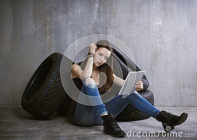 Young, slender girl is sitting near the tires and looking at the Stock Photo