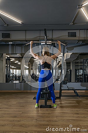 Young slender woman in tight leggings trains in the gym. Back view. Upper block thrust. Vertical frame Stock Photo