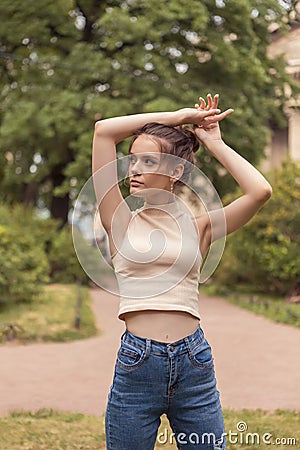 Young slender woman 18 years old stands in park with raised arms. Stock Photo