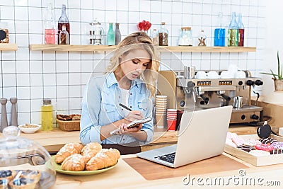 young small business owner taking notes and using laptop Stock Photo