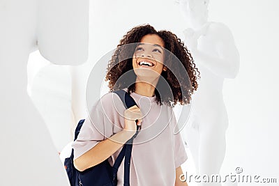 Young smiling african american female student in casual wear with backpack among plaster statues Stock Photo