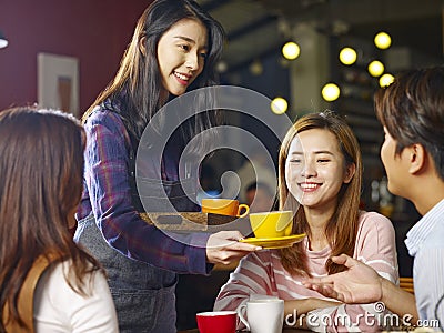Young smiling asian waitress serving coffee to customers Stock Photo