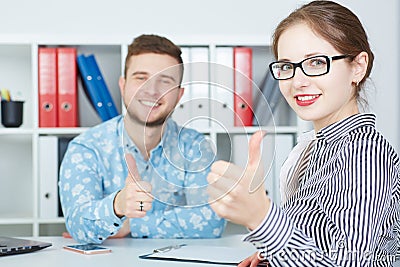 Young smiling business partners showing OK sign with thumbs up. Stock Photo