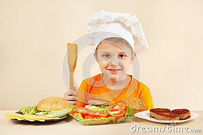 Young smiling chef at the table with ingredients is going to cook hamburger Stock Photo