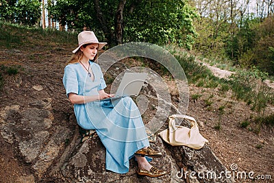 A young smiling girl freelancer works with a laptop in nature. Stock Photo