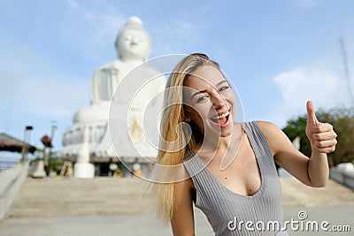 Young smiling girl showing thumbs up, white Buddha statue in Phuket in background. Stock Photo
