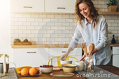 Young smiling housewife standing in kitchen near table is cooking dinner, cleaning dishes. Girl is making breakfast Stock Photo