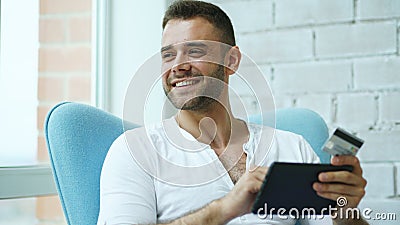 Young smiling man doing online shopping using digital tablet computer sitting at balcony at home Stock Photo