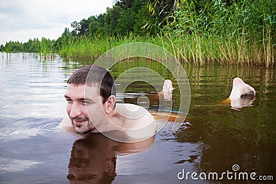 Young smiling man swimming in the water on background of grassy shore Stock Photo