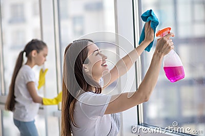 Young smiling mom and daughter washing a window. Stock Photo