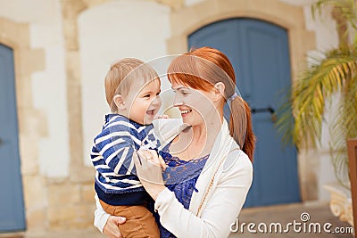 Young smiling mother holding smiling baby boy in the striped jacket Stock Photo