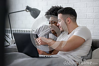 Young smiling multi ethnic couple shopping over internet in the bed in the morning Stock Photo