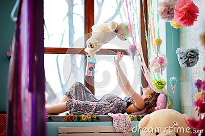 A young, smiling, pregnant girl lies on the windowsill and plays Stock Photo