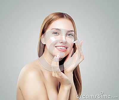 Young smiling woman applying cream on her healthy skin. Female face. Facial treatment and skin care concept Stock Photo