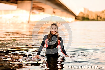 Young smiling woman in black wetsuit stands in the water. Stock Photo