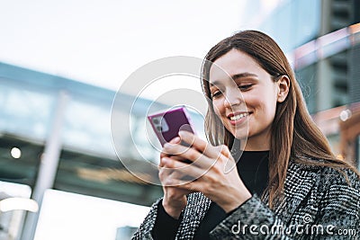 Young smiling woman in coat using mobile phone in evening city street Stock Photo