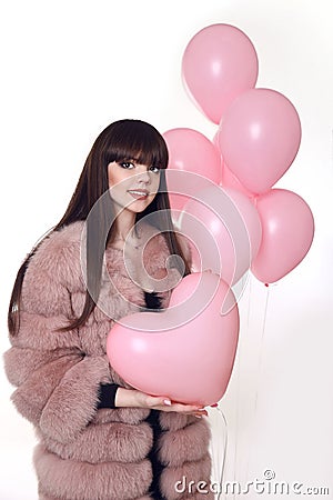 Young smiling woman in fashion fur coat holding pink heart over Stock Photo