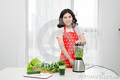 Young smiling woman making smoothie with fresh greens in the blender in kitchen at home. Healthy vegetarian smoothie for weight l Stock Photo