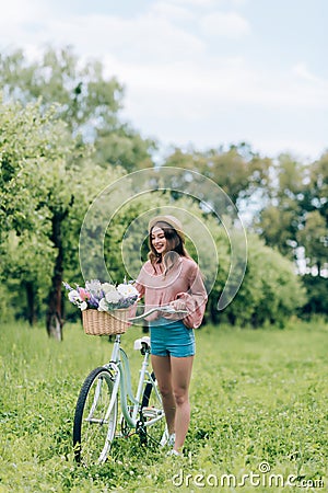 young smiling woman with retro bicycle with wicker basket full of flowers Stock Photo