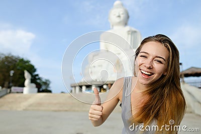Young smiling woman showing thumbs up, white Buddha statue in Phuket in background. Stock Photo