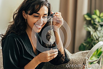 Young smiling woman sitting on a couch applying hyaluronic acid on a face Stock Photo