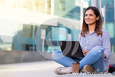 Young smiling woman using computer and drinking coffee outdoors with copy space Stock Photo