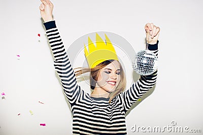 Young smiling woman on white background celebrating party, wearing stripped dress and yellow paper crown, happy dynamic Stock Photo