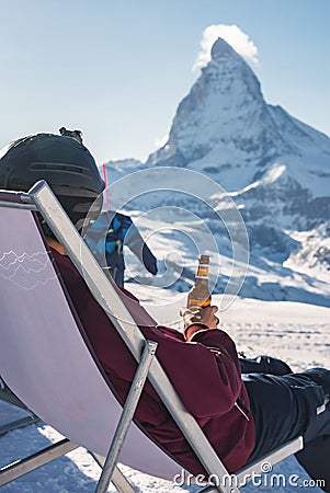 Young snowboarder cheering with a beer after skiing day in a bar or a cafe at the Zermatt ski resort Stock Photo