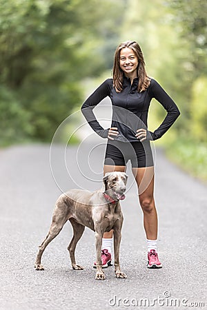 Young sporting woman and her Weimaraner dog stand together in the forest. Stock Photo