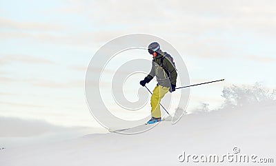 Skier descending from snow-covered high mountain top. Extreme skiing concept. Mountains view. Winter sky on background. Stock Photo