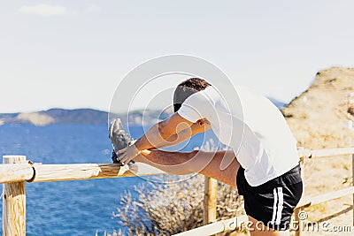 Young sportsman stretching his legs outdoors while looking at the horizon with the sea to the side Stock Photo