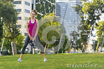 Young sportswoman performing exercises on the grass in a city Stock Photo