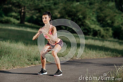 Young sporty woman doing squat exercises with rubber band outdoor. Stock Photo