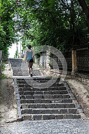 Young sporty woman in sportswear running up steep cobblestone stairs in green alley Stock Photo