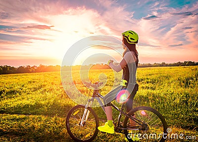 Young sporty woman watching the sunset on a bicycle. Sporty girl on bike stopped to enjoy the moment at beautiful sunset Stock Photo
